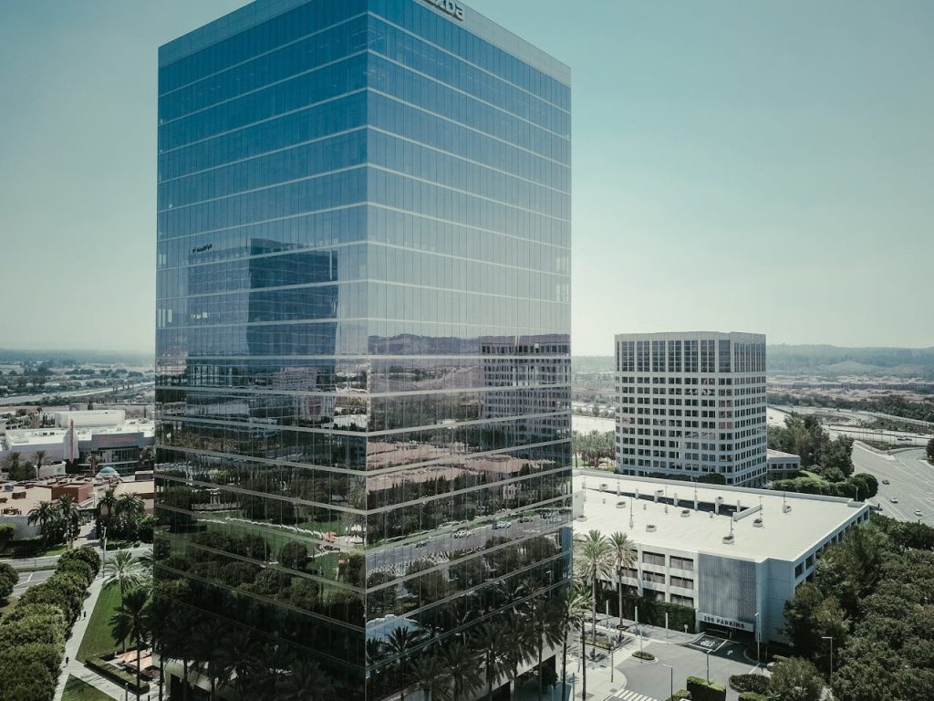 Tall glass skyscraper reflecting the cityscape in a modern urban setting under a clear sky.